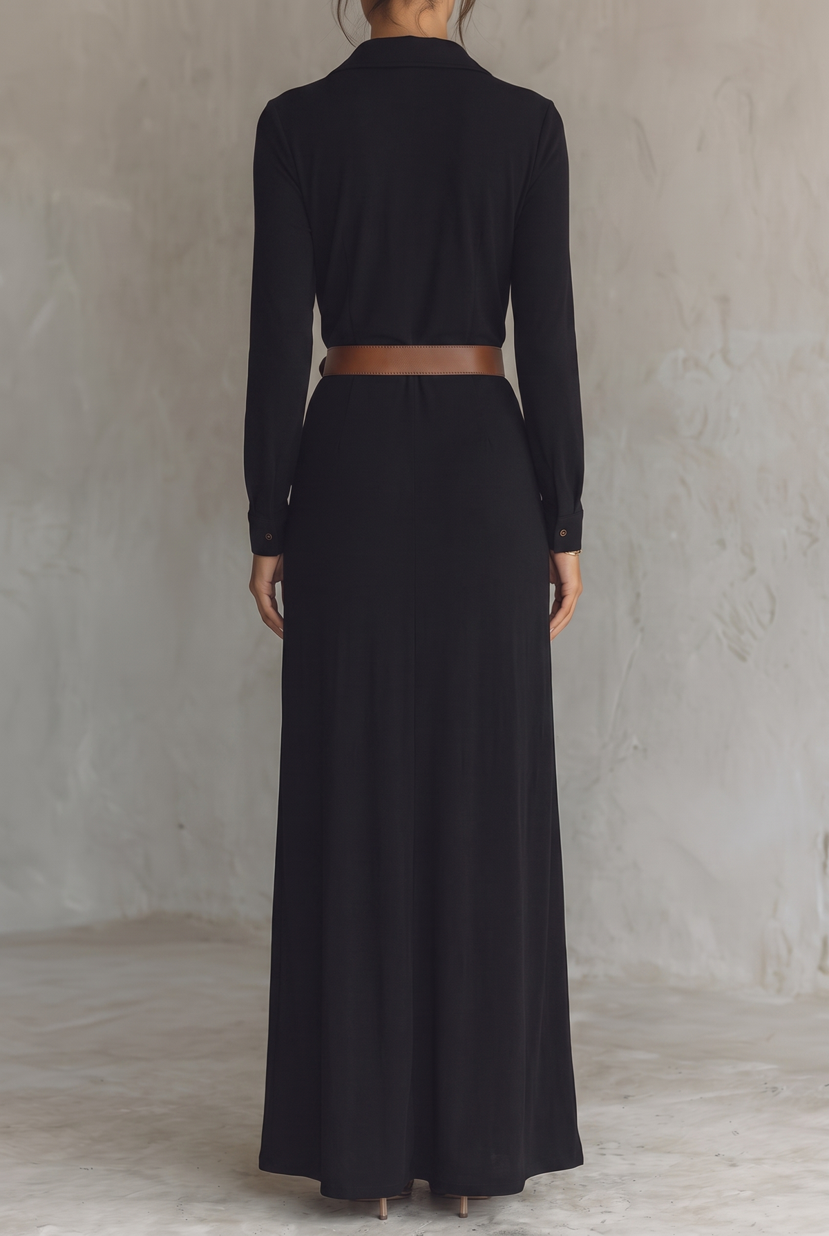 Back view of the black maxi dress, plain smooth back, long sleeves with button cuffs and brown belt at the waist. 15