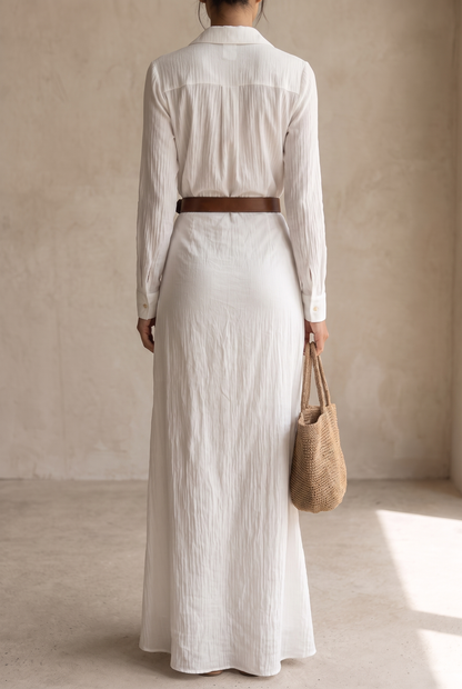 Back view of the white maxi dress, showing the pleated yoke, button cuffs, brown belt and straw tote held in one hand. 11