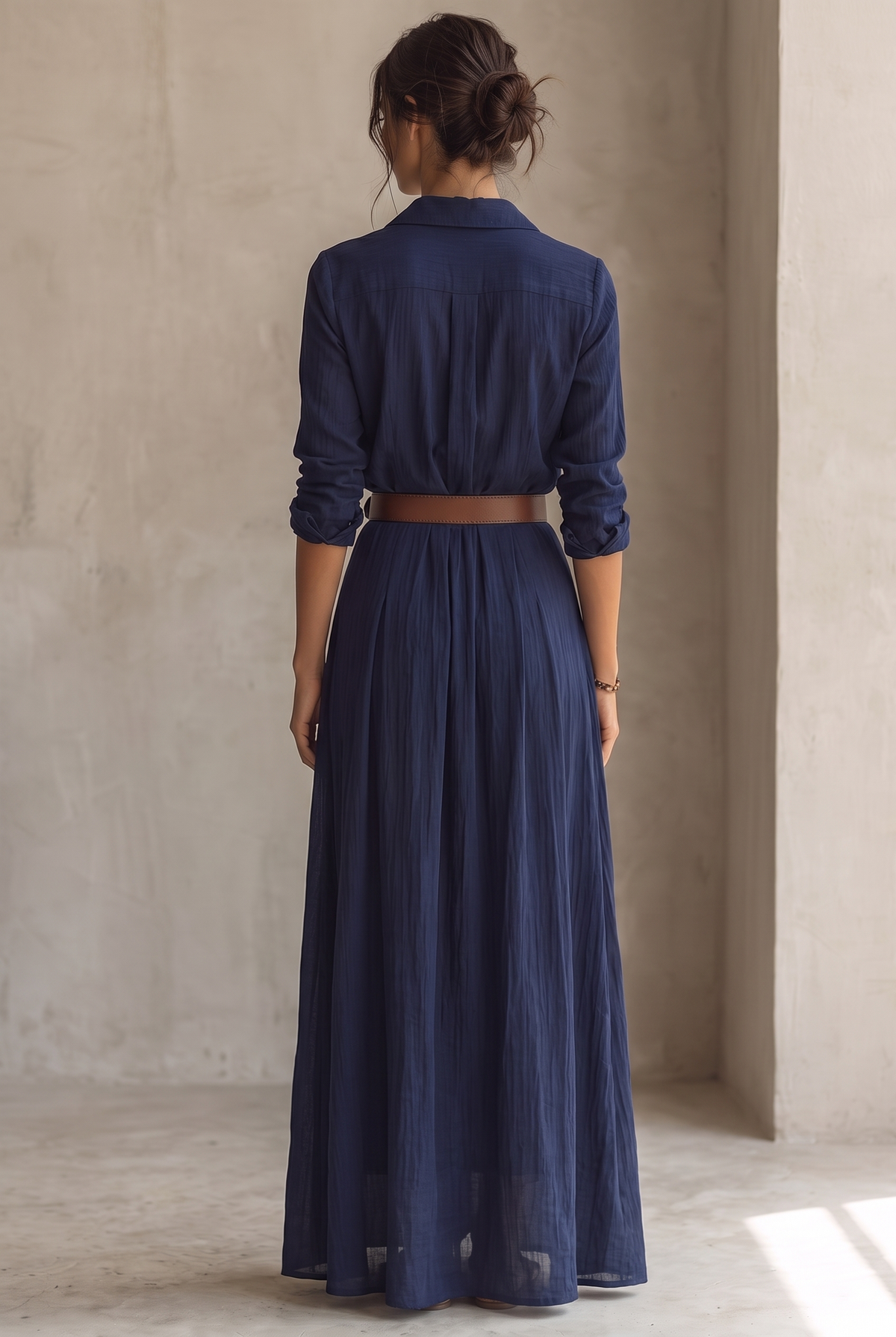 Back view of the navy blue maxi dress, with pleated back, collar, wide brown belt and rolled sleeves. 7