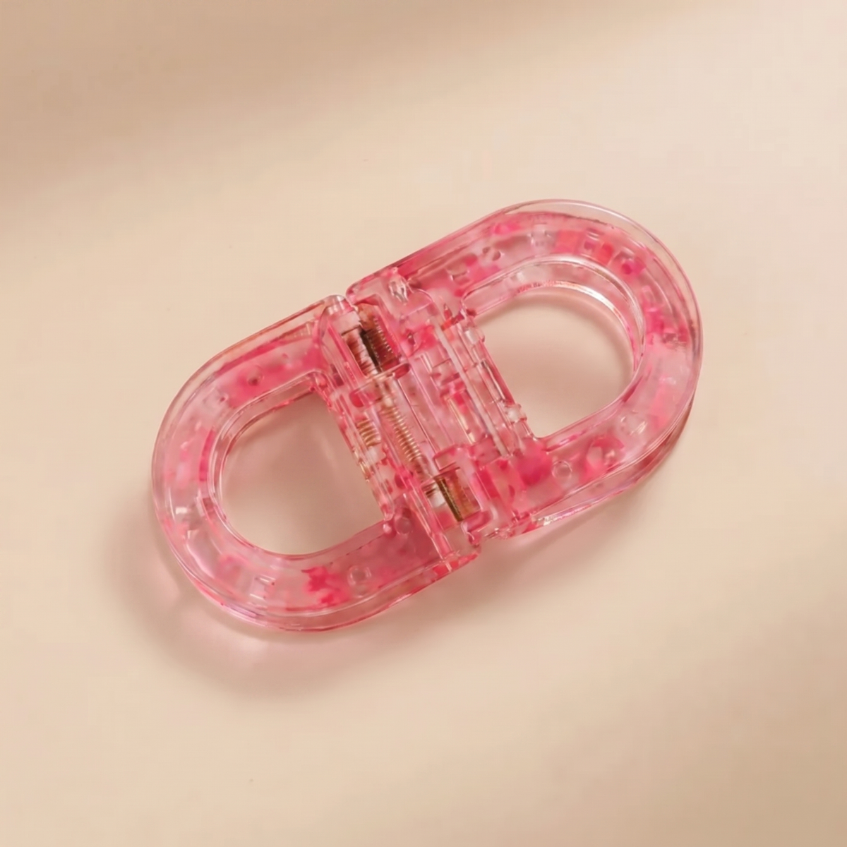 Translucent pink flat hair clip speckled with brighter pink, with a visible spring, photographed from above. 12