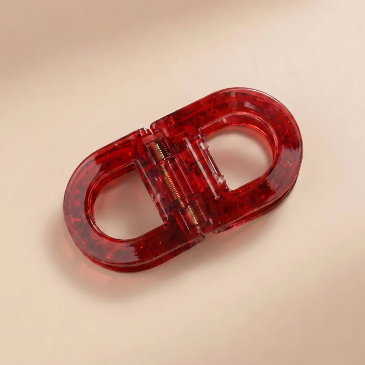 Translucent deep red flat hair clip with a visible gold-coloured spring, photographed from above on a beige background. 10