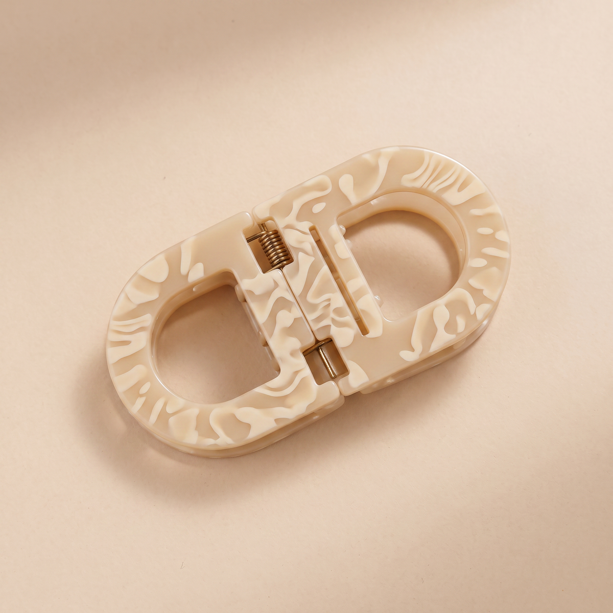 Flat hair clip in cream marbled resin with swirling pale patterns and a brass-coloured spring, shown from above. 11