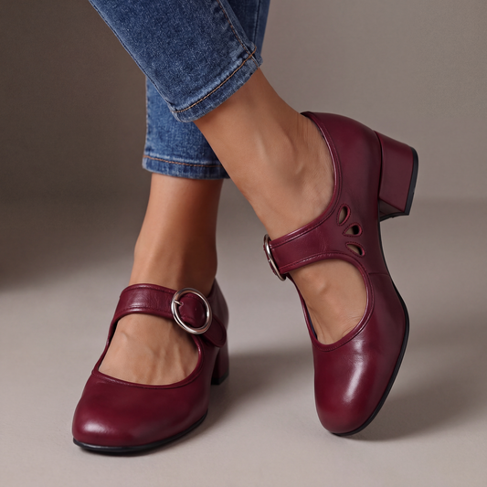 Burgundy leather block-heel pumps worn with cropped jeans, showing a round silver buckle strap and teardrop cut-outs on the side. 2