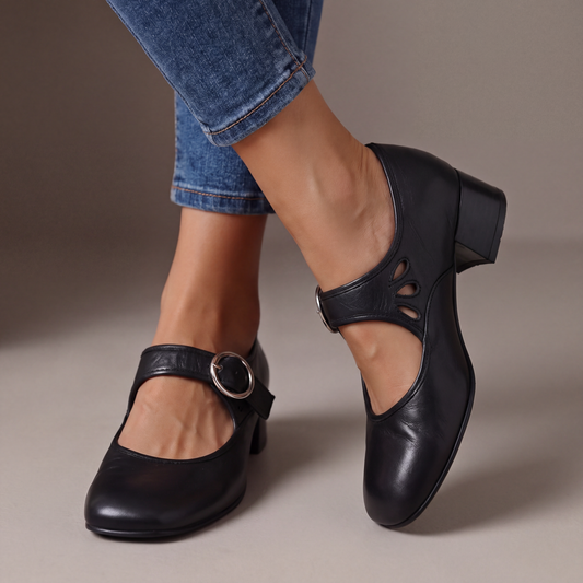 Black leather block-heel pumps worn with cropped jeans, showing a round silver buckle strap and teardrop cut-outs on the side. 1