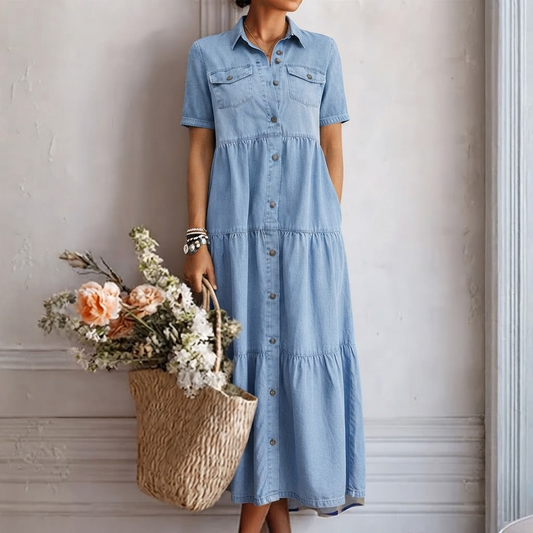 Model in the light blue tiered short-sleeved dress against a panelled wall, holding a woven basket of peach and white flowers. 1