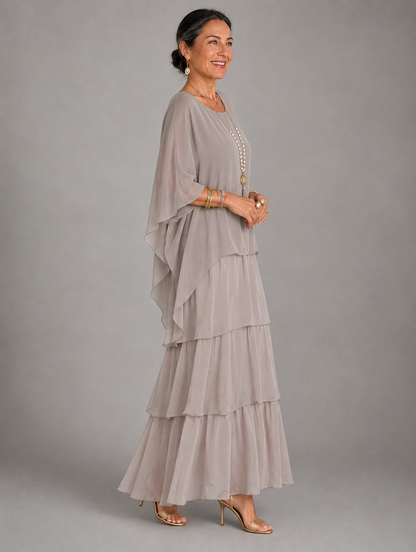 Side view of the taupe grey tiered chiffon maxi dress on a model, showing the flowing cape sleeve and layered skirt. 19