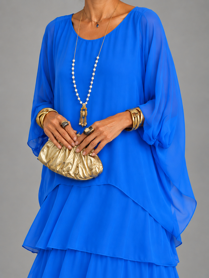 Upper body detail in royal blue, showing the sheer draped sleeves and layered chiffon top, held with a gold clutch. 27