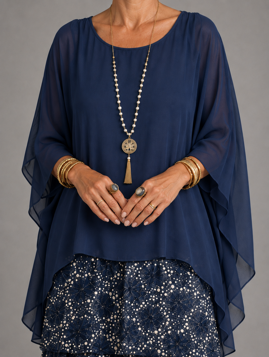 Close-up of a navy sheer chiffon overlay with flowing sleeves, worn with a long pendant necklace over a dotted tiered skirt. 45