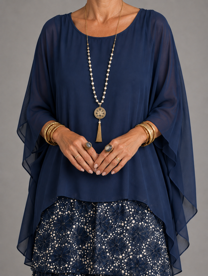 Close-up of a navy sheer chiffon overlay with flowing sleeves, worn with a long pendant necklace over a dotted tiered skirt. 45