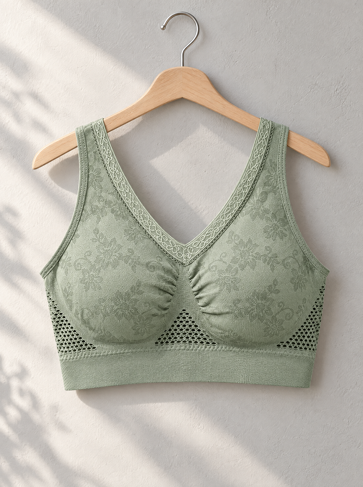 Sage green bra hanging on a wooden hanger against a sunlit wall 4