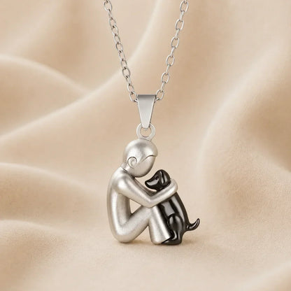 Matt silver-toned seated figure hugging a small glossy black dog, shown from the side on cream fabric 7