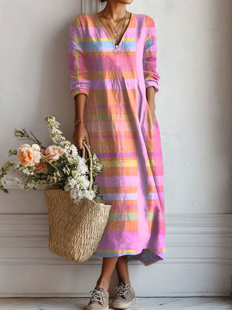 Model wearing a long-sleeved, V-neck midi dress in pink, orange and blue stripes, with a hand in the pocket, holding a woven flower basket. 1