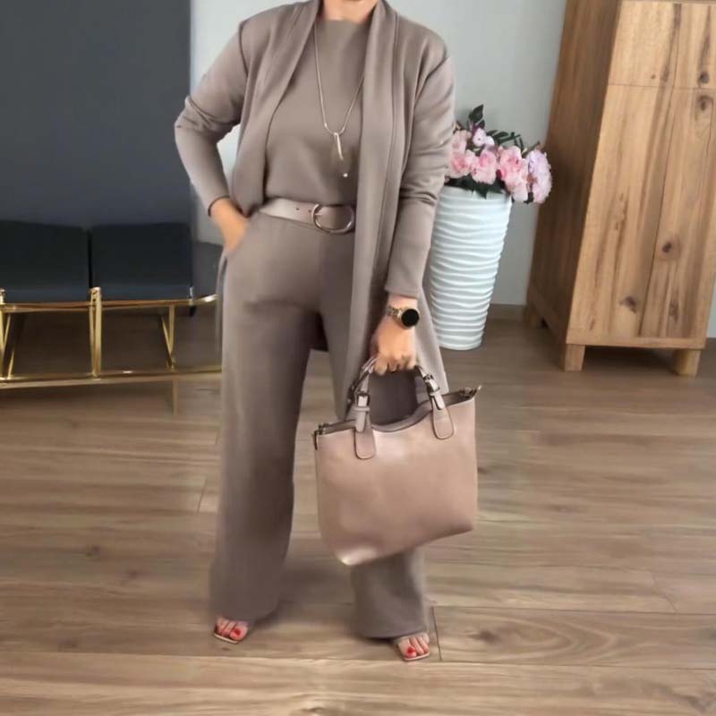 Woman in a taupe cardigan, top and wide-leg trousers with belt and pendant necklace, holding a blush-pink handbag. 10