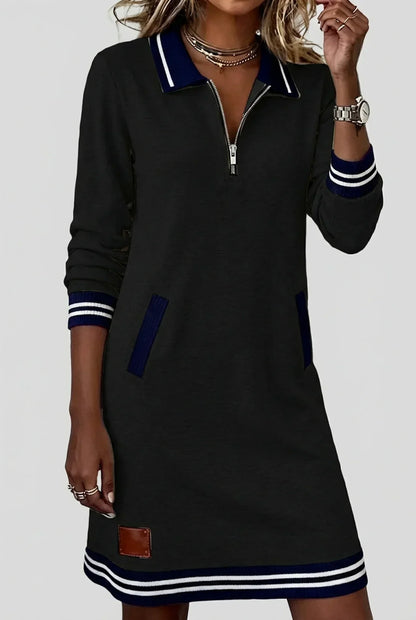 Model wearing the black dress with navy and white striped collar, cuffs and hem, one hand raised near her necklace. 4