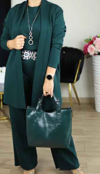Woman in a dark green cardigan, top and wide-leg trousers with a decorative belt, ring necklace and matching green handbag. 17