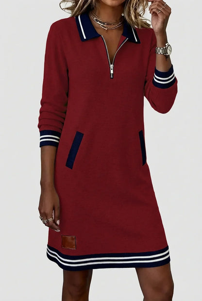 Model wearing the burgundy dress with one hand raised to her necklace, showing the half-zip collar and striped hem. 12