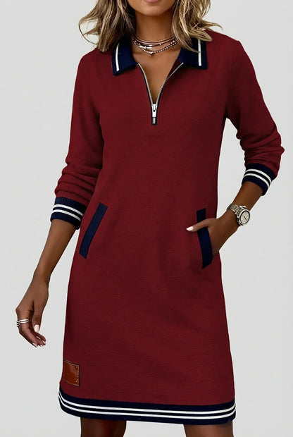Model in the burgundy red dress with contrasting navy striped collar, cuffs and hem, one hand in a pocket. 5