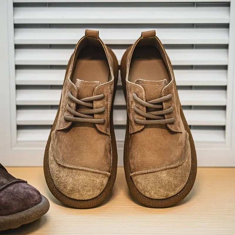 Pair of tan suede lace-up shoes with wide rounded toe caps and thick crepe-style soles, standing in front of white shutters. 1