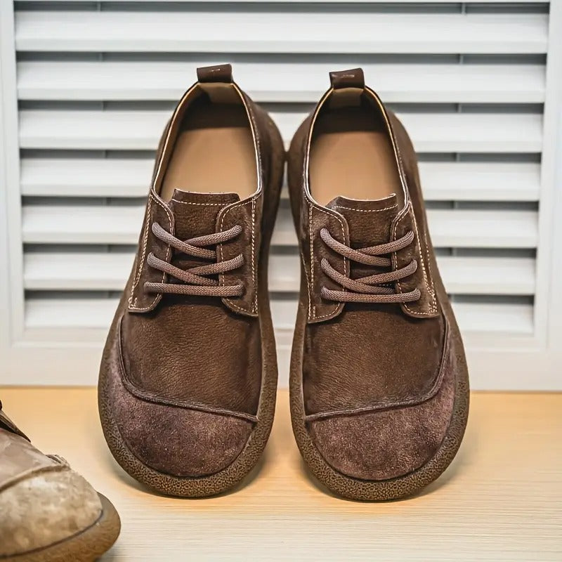 Pair of dark brown lace-up shoes with contrast stitching and thick soles, standing in front of white shutters. 10