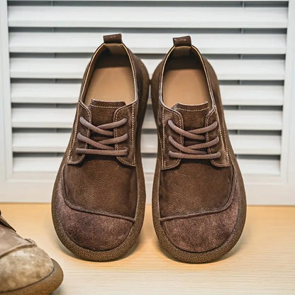 Pair of dark brown lace-up shoes with contrast stitching and thick soles, standing in front of white shutters. 10