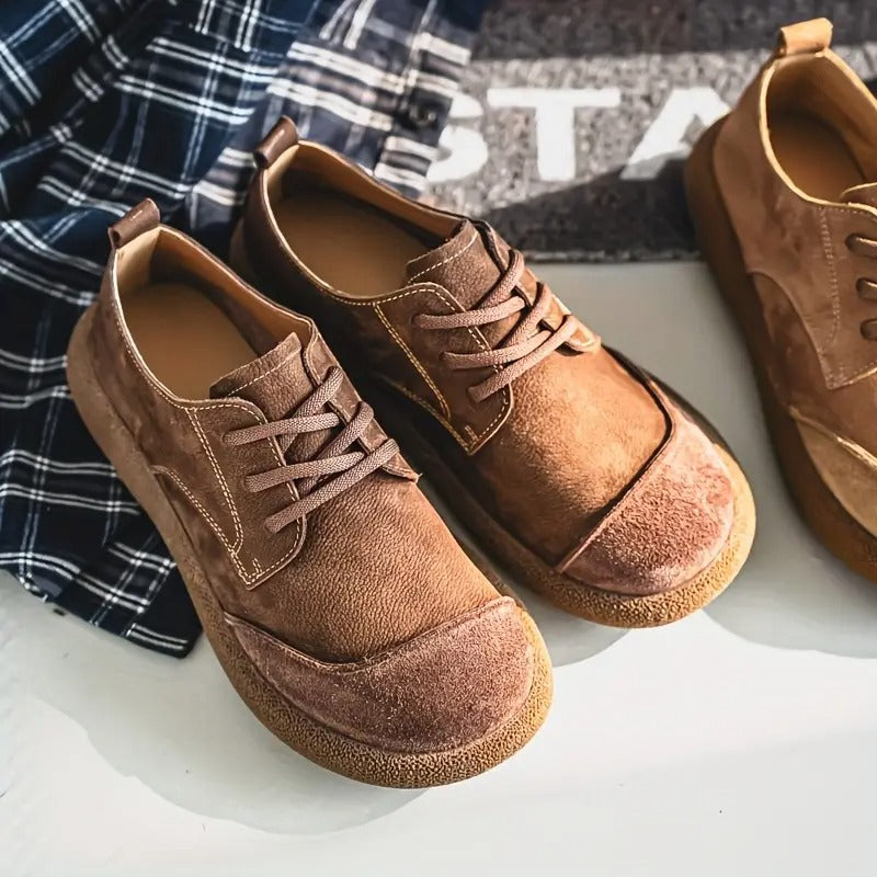 Brown lace-up shoes with suede toe caps and crepe soles resting on a white surface beside a navy checked shirt. 11