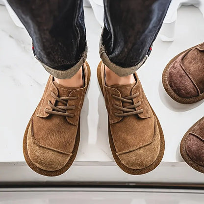 Top-down view of tan lace-up shoes worn with rolled dark jeans, showing the broad toe shape, with brown pairs alongside. 4