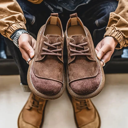 Hands holding up a pair of brown suede lace-up shoes, with tan pair on the floor below. 9