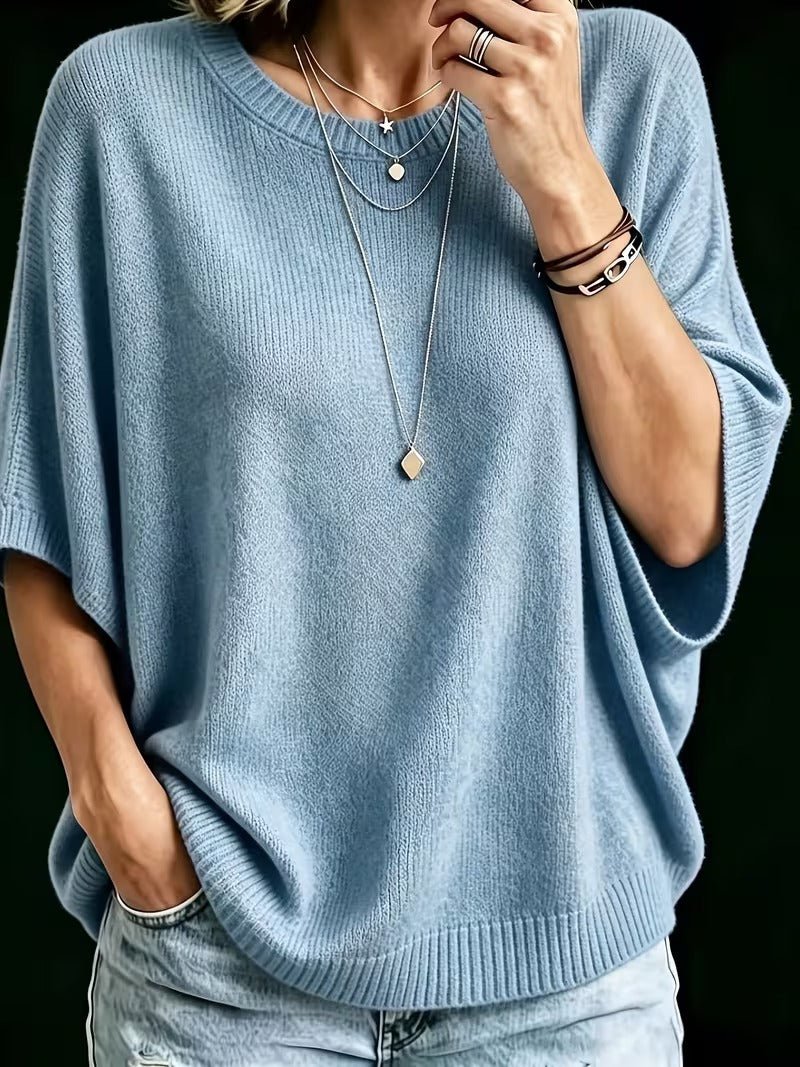Close-up of the light blue knit batwing top with layered necklaces, one hand raised to the chin. 12