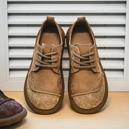 Pair of light tan lace-up shoes with a rounded toe, shown front-on in front of shutters 7