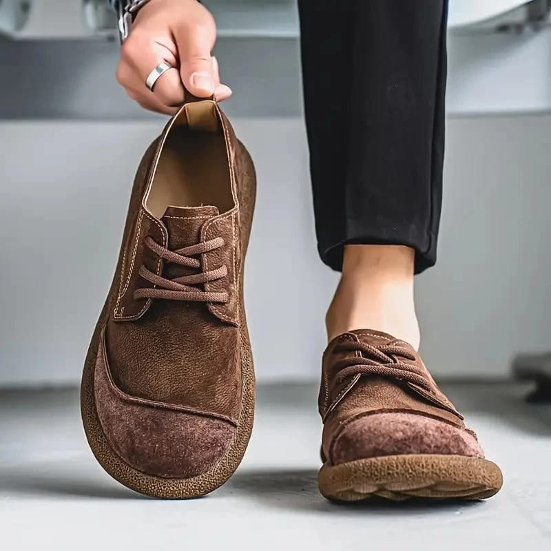 Brown lace-up shoe lifted by the heel tab beside the other worn with black trousers 8