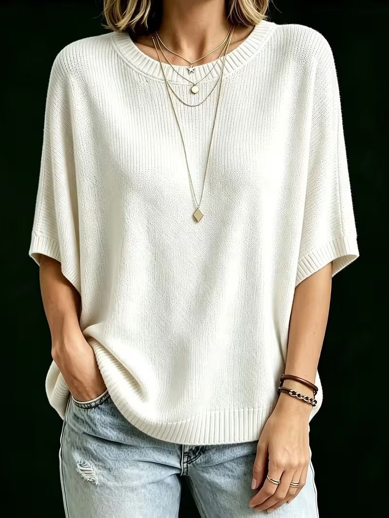 Cream knit batwing top worn on a model with one hand in a pocket, showing loose draped sleeves and ribbed hem. 24