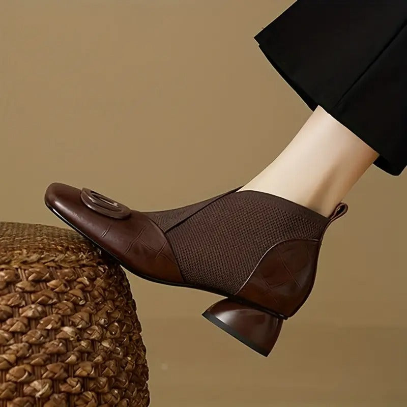 Side view of a brown leather and knit ankle boot with buckle and rounded heel, worn with black trousers 1