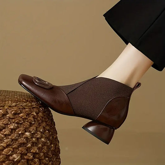 Side view of a brown leather and knit ankle boot with buckle and rounded heel, worn with black trousers 1