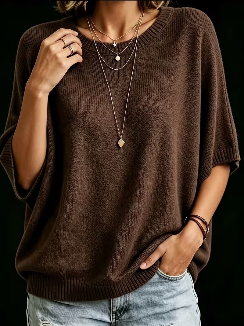 Dark brown knit top worn with one hand touching the collarbone and the other in a pocket, with layered gold necklaces. 20