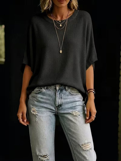 Black knit batwing top styled with distressed light-wash jeans and layered necklaces, shown from the front to the thighs. 27