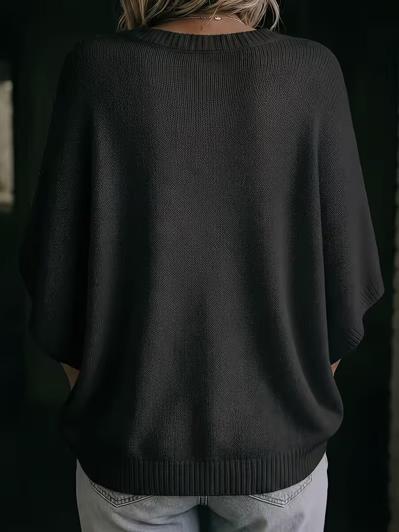 Back view of the black knit batwing top on a model, showing the ribbed neckline, wide sleeves and curved ribbed hem. 28