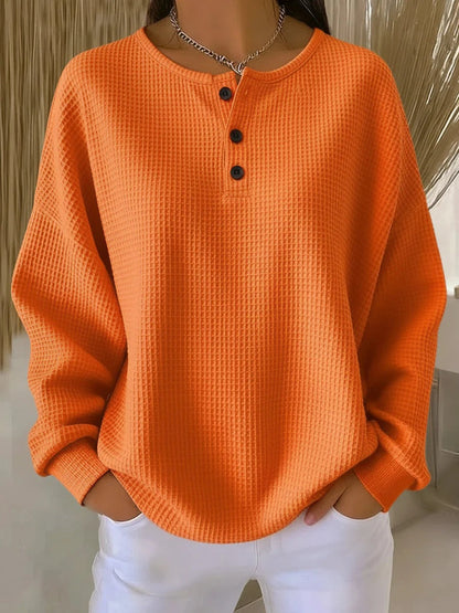 Plain bright orange waffle knit henley jumper with three dark buttons, worn with white trousers 7