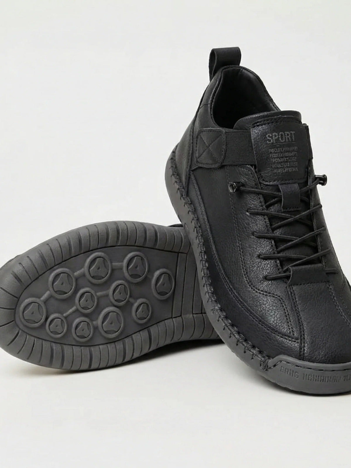 Black trainers with grey rubber sole, one shoe leaning on the other to show the studded tread 1