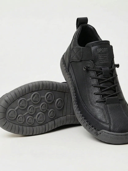 Black trainers with grey rubber sole, one shoe leaning on the other to show the studded tread 1