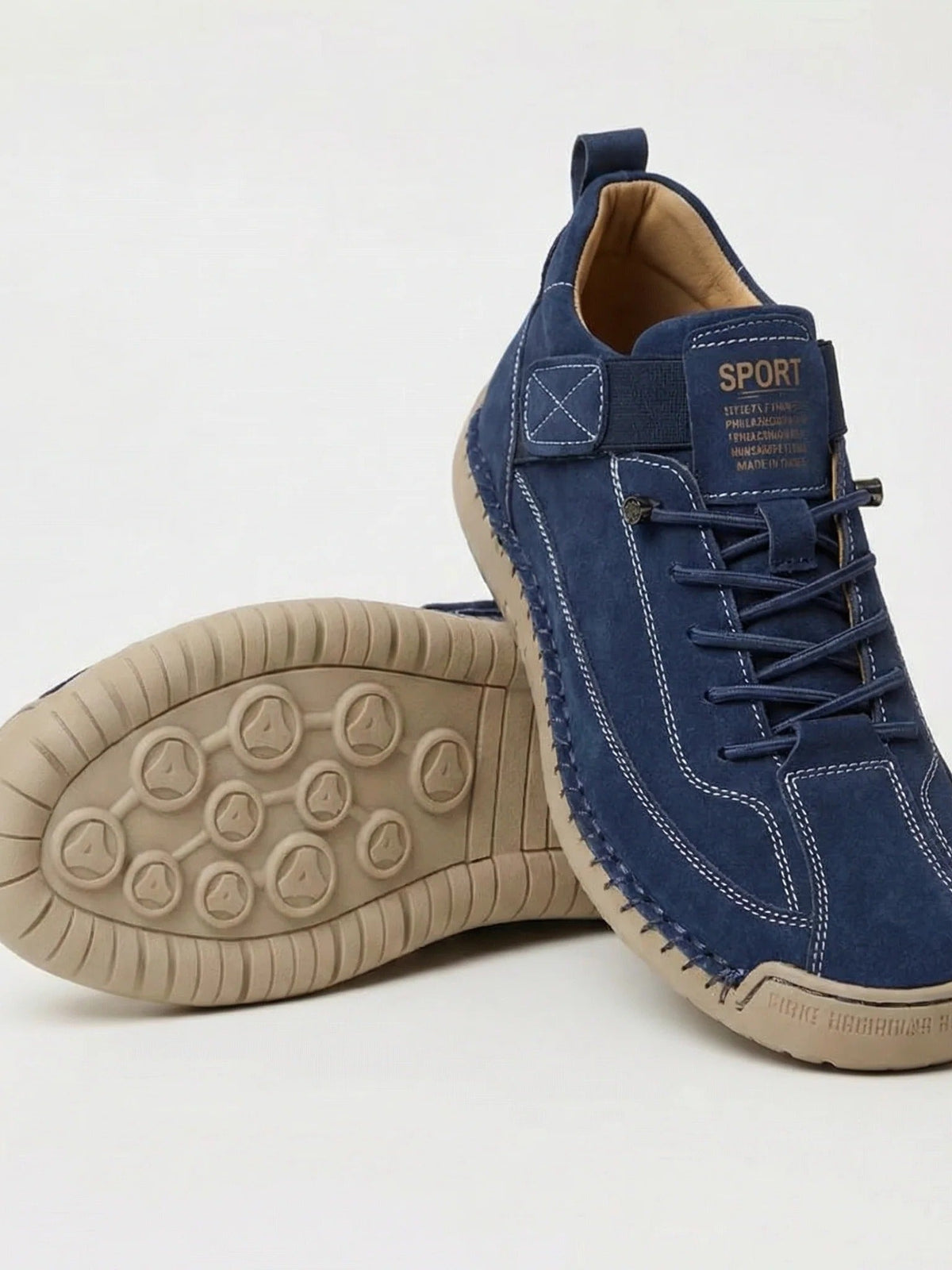 Navy suede trainers with white contrast stitching and a tan sole, one showing its patterned tread 2