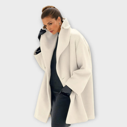 Model in the coat in cream with a high wide lapel, worn over a dark dress and black gloves. 6