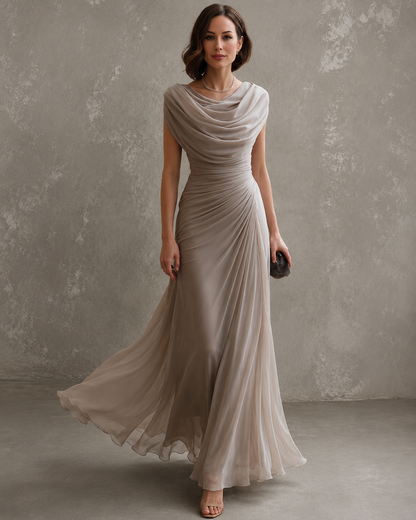 Model in the taupe-grey chiffon maxi dress with a draped cowl neckline and ruched waist, skirt flowing as she walks, holding a clutch. 1