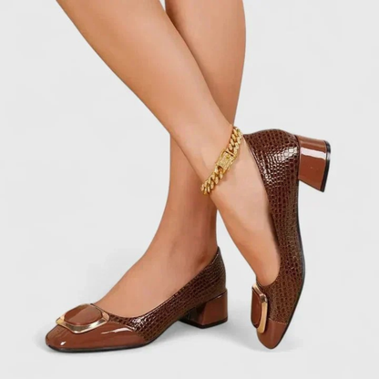 Model with crossed legs wearing brown croc-effect loafers, showing the gold-trimmed toe ornament and low block heel. 4