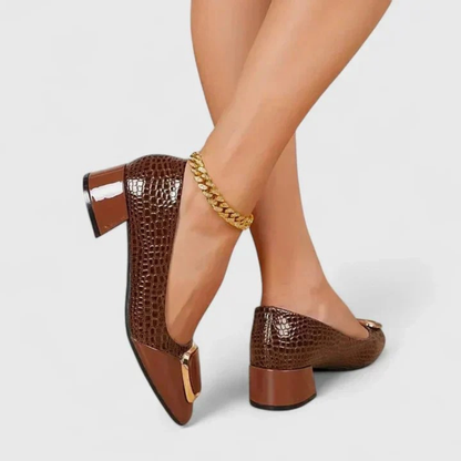 Side and heel view of brown croc-effect block-heel loafers worn with crossed legs and a gold ankle chain. 3