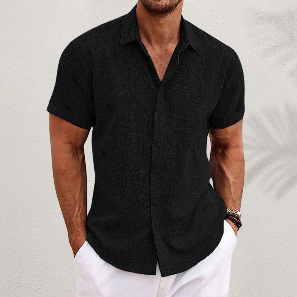 Black textured short-sleeved shirt with cuffed sleeves, worn by a model with white trousers against a pale wall. 4