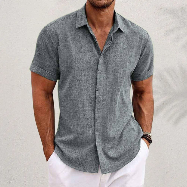 Grey textured short-sleeved shirt with cuffed sleeves, worn by a model with white trousers against a pale wall. 5