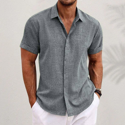 Grey textured short-sleeved shirt with cuffed sleeves, worn by a model with white trousers against a pale wall. 5