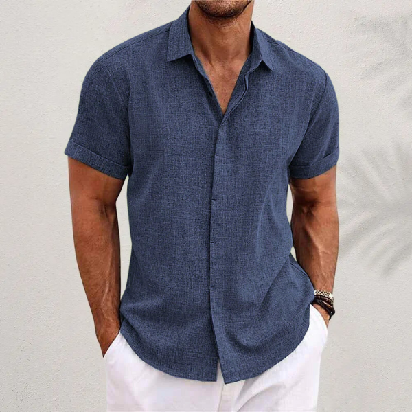 Navy blue textured short-sleeved shirt with cuffed sleeves, worn by a model with white trousers against a pale wall. 6