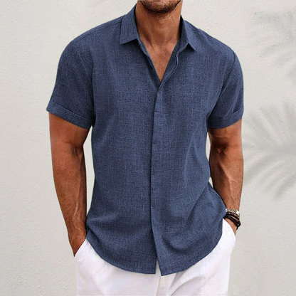 Navy blue textured short-sleeved shirt with cuffed sleeves, worn by a model with white trousers against a pale wall. 6