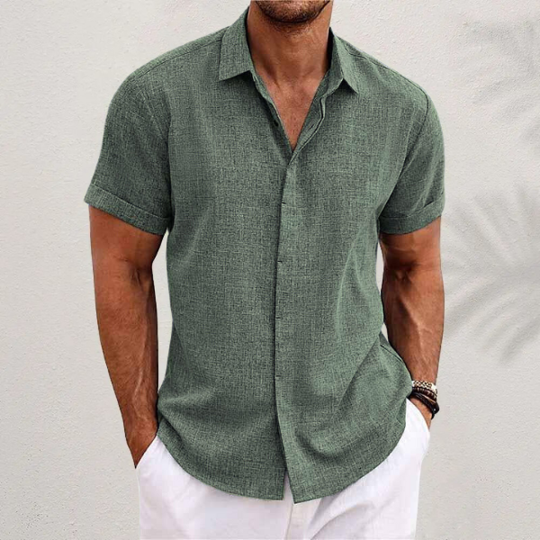 Sage green textured short-sleeved shirt with cuffed sleeves, worn by a model with white trousers against a pale wall. 7